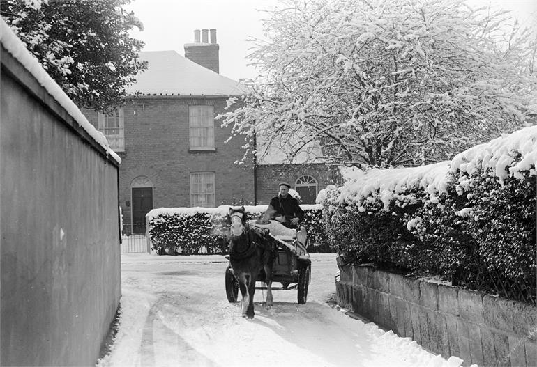 Photograph. Bill Nash on Milk Float on Bank Loke, North Walsham in snow (North Walsham Archive).