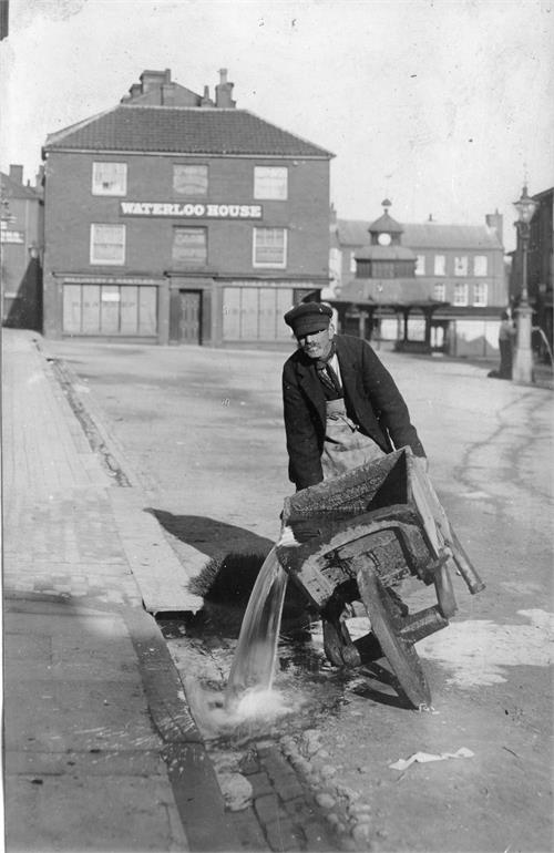 Photograph. Bruff Hewitt flushing the surface drains in the North Walsham Market Place (North Walsham Archive).