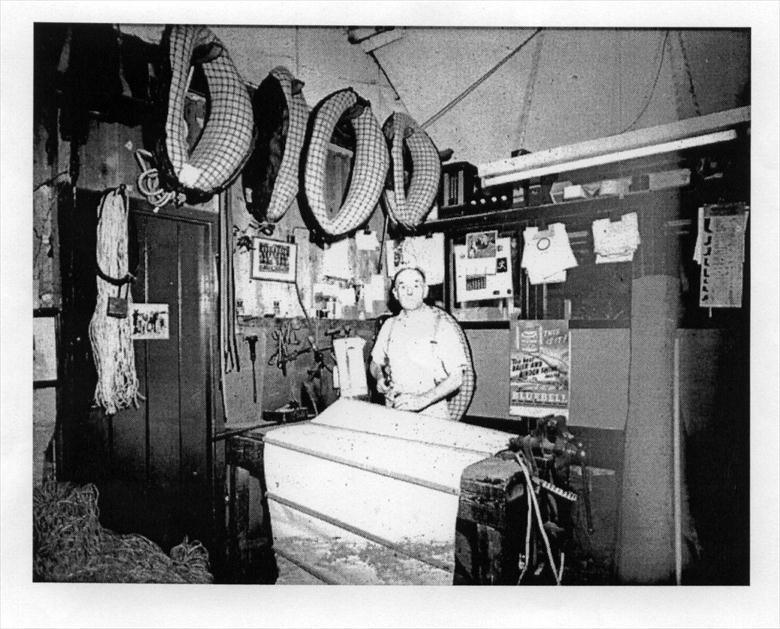 Photograph. John Hewitt, Saddler, Church Plain, Vicarage Street, North Walsham. Repairing a reaper sail on belt. (North Walsham Archive).