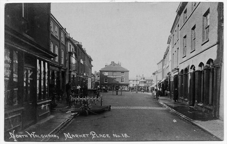 Photograph. North Walsham Market Place, looking west. Note brick pathway to cross the muddy road. (North Walsham Archive).